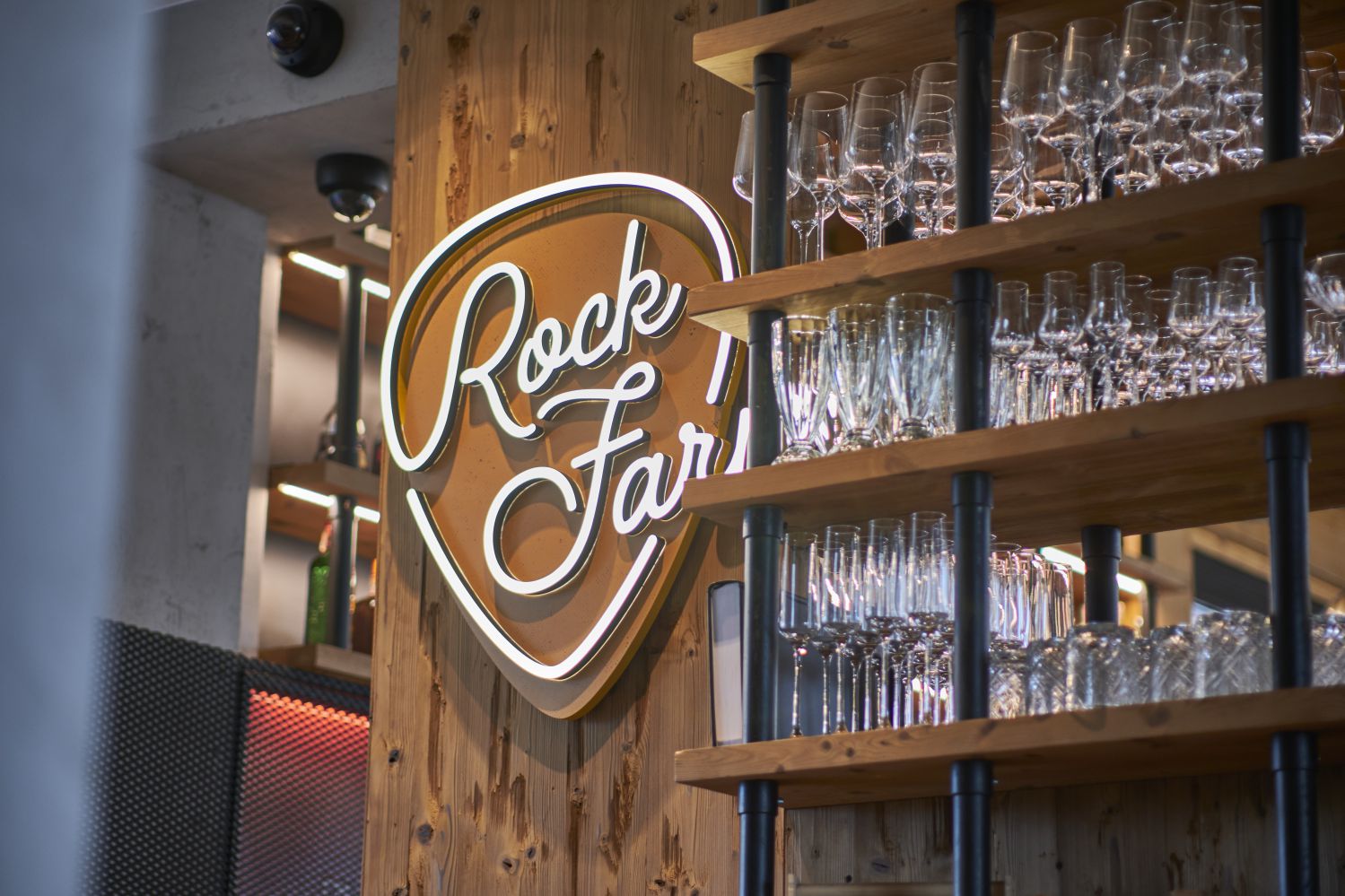 Blog-Rock-Farm-logo-behind-the-bar Rock farm logo behind bar on wooden wall by shelving with glasses on.