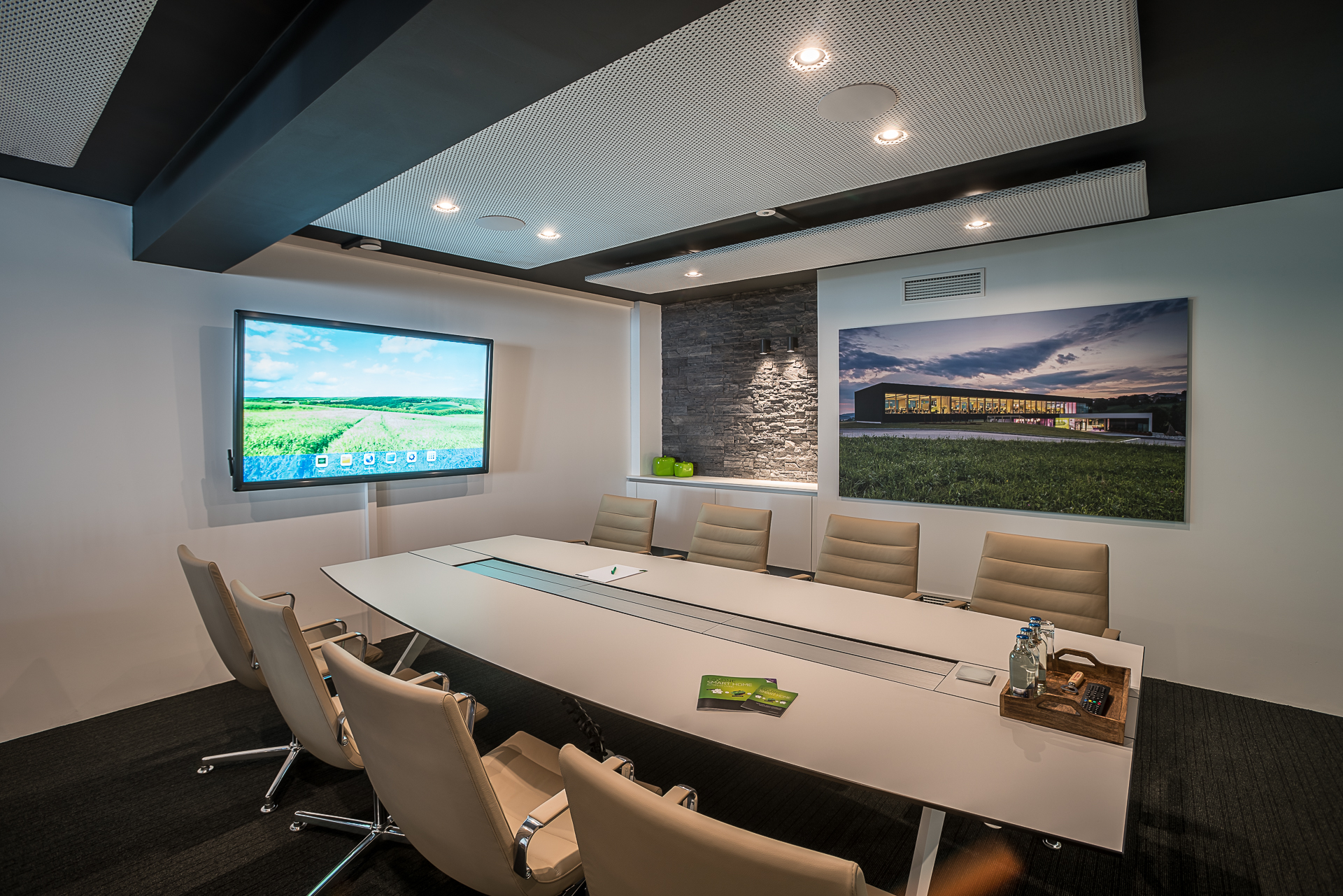 een kantoorruimte met een grote witte tafel en 8 zitplaatsen, en een groot scherm tegen de muur.