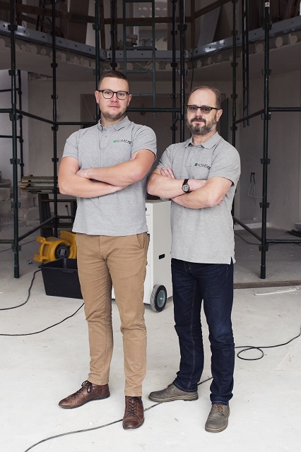 Dwóch uśmiechniętych mężczyzn stoi obok siebie z założonymi rękami